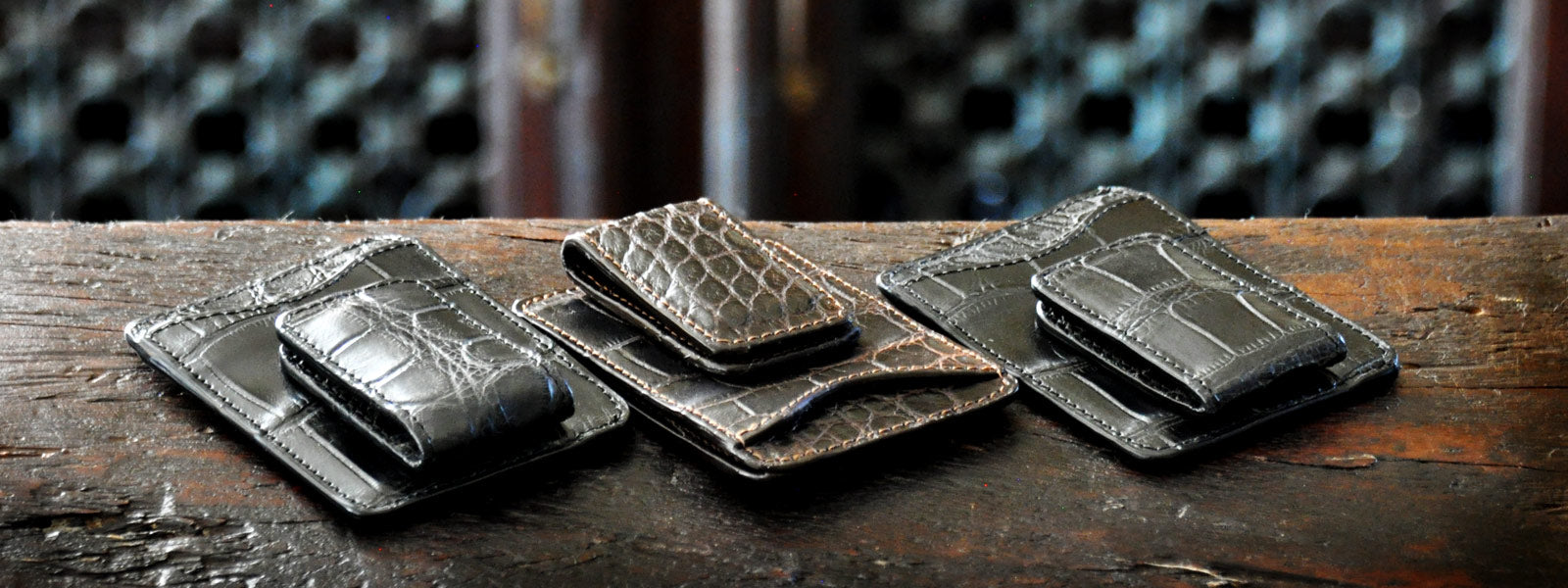American Alligator leather wallets and money-clips produced by Borlino in Italy one a wood table. 