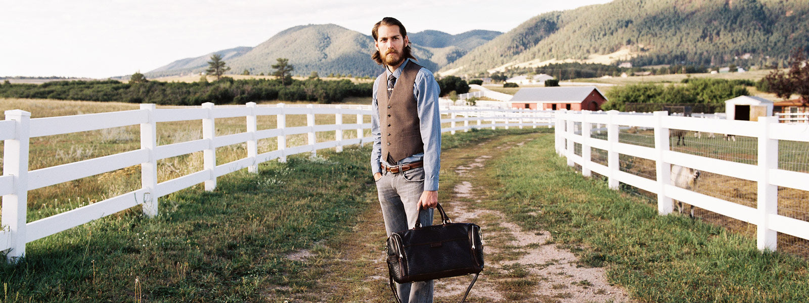 Gentleman carrying a handcrafted Italian leather travel bag along a rustic Tuscan countryside path, exuding timeless luxury.